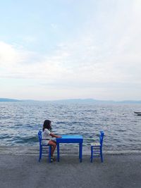 Girl sitting on chair at beach against sky