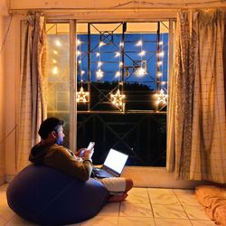 Midsection of woman using mobile phone while sitting on window