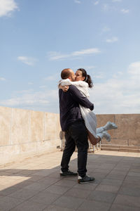 Rear view of man and woman with umbrella against sky