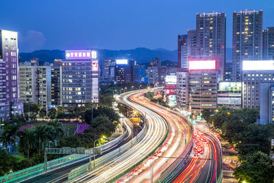 High angle view of light trails on road amidst buildings in city at night