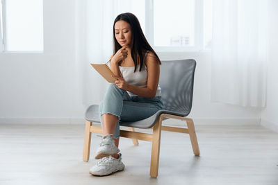 Sad young woman with book sitting on chair