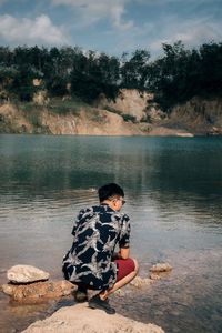 Boy sitting on rock by lake