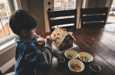 High angle view of boy making gingerbread house on wooden table during christmas at home