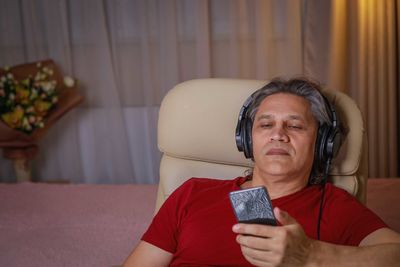 50-year-old man listens to music on headphones at home, sitting in a chair. relaxing delight.