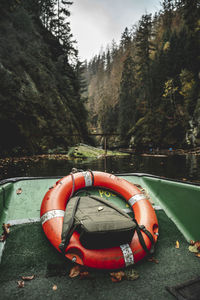 Orange rescue floating device on green boat surrounded by green cliffs ans trees