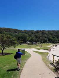 Rear view of man walking on landscape against clear blue sky