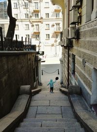 Rear view of girl walking on steps amidst buildings in city