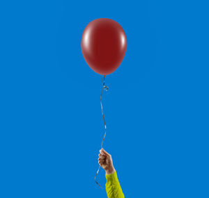 Hand holding balloon against clear blue sky