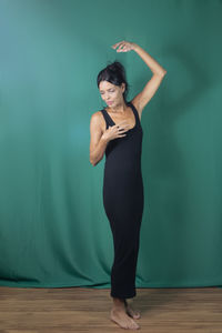 Portrait of standing adult model in black dress against dark green background. 