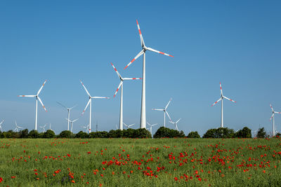 Windmills on field against clear blue sky