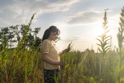 Side view of woman standing amidst plants on field against sky
