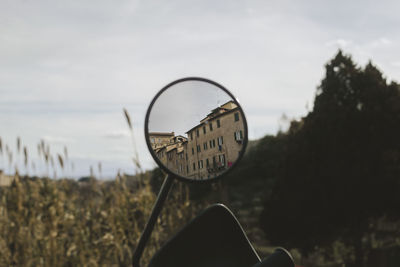 Close-up of side-view mirror against sky