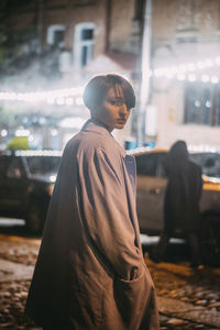 Side view of young man looking away while standing on street in city