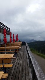 Closed red parasols by empty seats and tables at cafe against cloudy sky