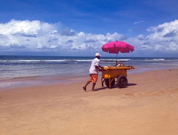 Vendor pushing concession cart at beach against sky