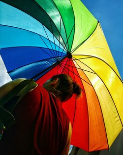 Low angle rear view of woman under colorful umbrella during sunny day