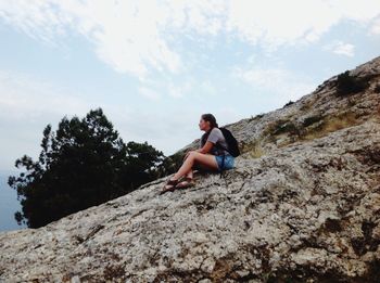 Full length of woman sitting on rock against sky