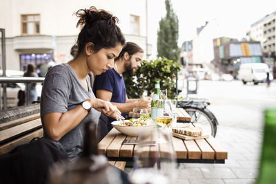Side view of man and woman having lunch at sidewalk cafe in city