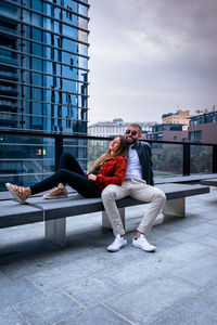 Man sitting with woman in background against sky in city