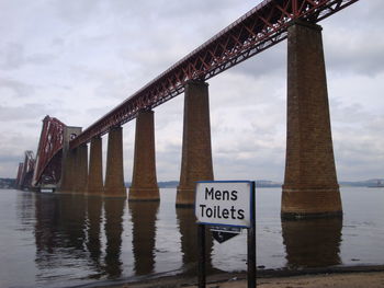 Information restroom sign next to bridge over river against sky