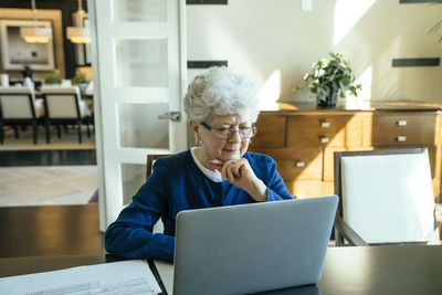 Serious senior woman using laptop computer at home