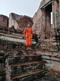 Low angle view of portrait monk standing with umbrella in temple