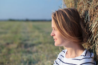 Side view of young woman leaning on hay bale at field