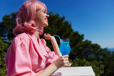 Smiling woman holding cocktail against trees