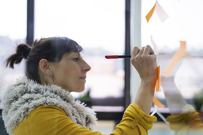 Businesswoman writing on window in creative office seen through glass