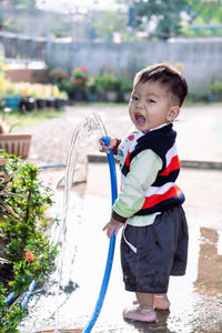 Adorable asian toddler boy plays and enjoys having fun watering garden flowers and lawn 