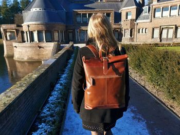 Rear view of woman walking on footpath against building in city