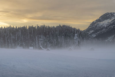 Snow covered landscape against sky during sunset