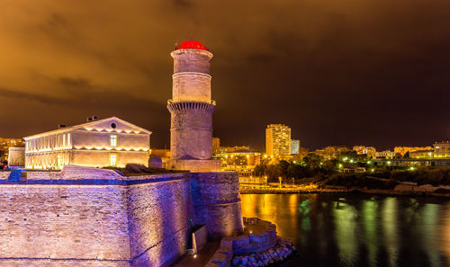 Illuminated factory by river against sky at night