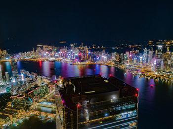 High angle view of illuminated city by sea against sky at night