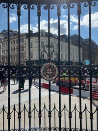 Metal gate of buildings against cloudy sky