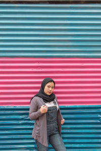 Portrait of young woman standing against red shutter