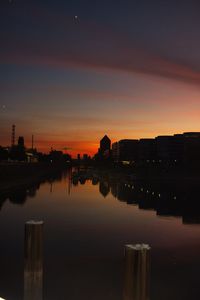 Silhouette buildings by lake against sky during sunset
