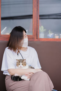 Asian woman wearing protective mask sit and play with her cat at outdoor coffee shop