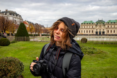 Young girl with camera posing in front of schloss belvedere in vienna. 