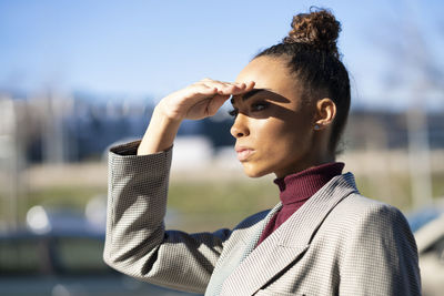 Young businesswoman shielding eyes while standing outdoors on sunny day