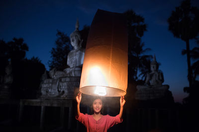 Portrait of woman by illuminated trees against sky at night