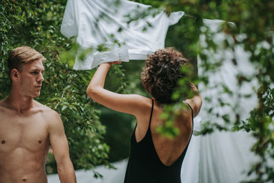 Rear view of shirtless man with woman standing by plants