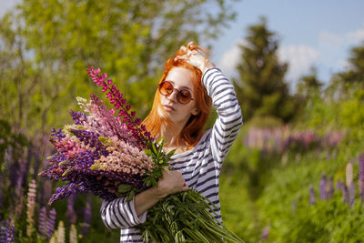 Young woman in the field of flowers with bunch of lupines