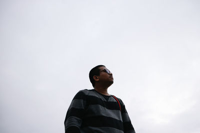 Low angle view of boy looking away against sky