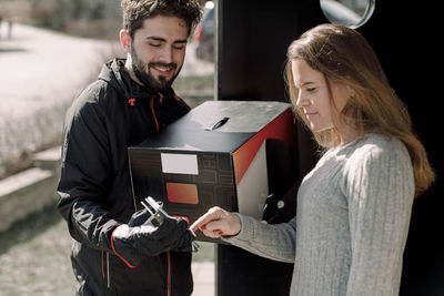 Female customer signing on mobile phone while receiving package from delivery man