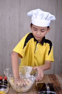 Boy wearing chef hat kneading dough in bowl at home