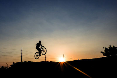 Silhouette man performing stunt on bicycle during sunset