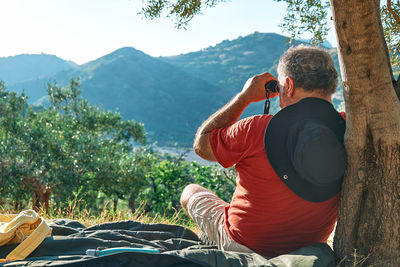 Rear view of tourist man looking through binoculars at the mountains view. hiking, unity with nature