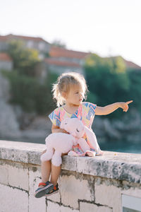 Portrait of smiling girl sitting on retaining wall