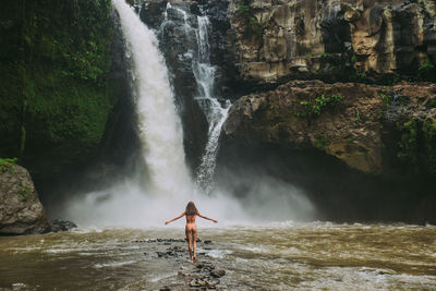 Young woman standing against waterfall